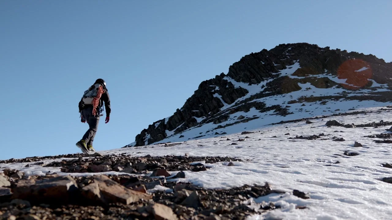 A hiker walking across a rocky, snow-covered alpine ridge in the Aurora commercial.