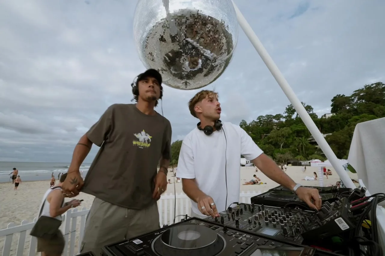 Two DJs beside their decks beneath a mirrored ball on the beach at Sandiscco.