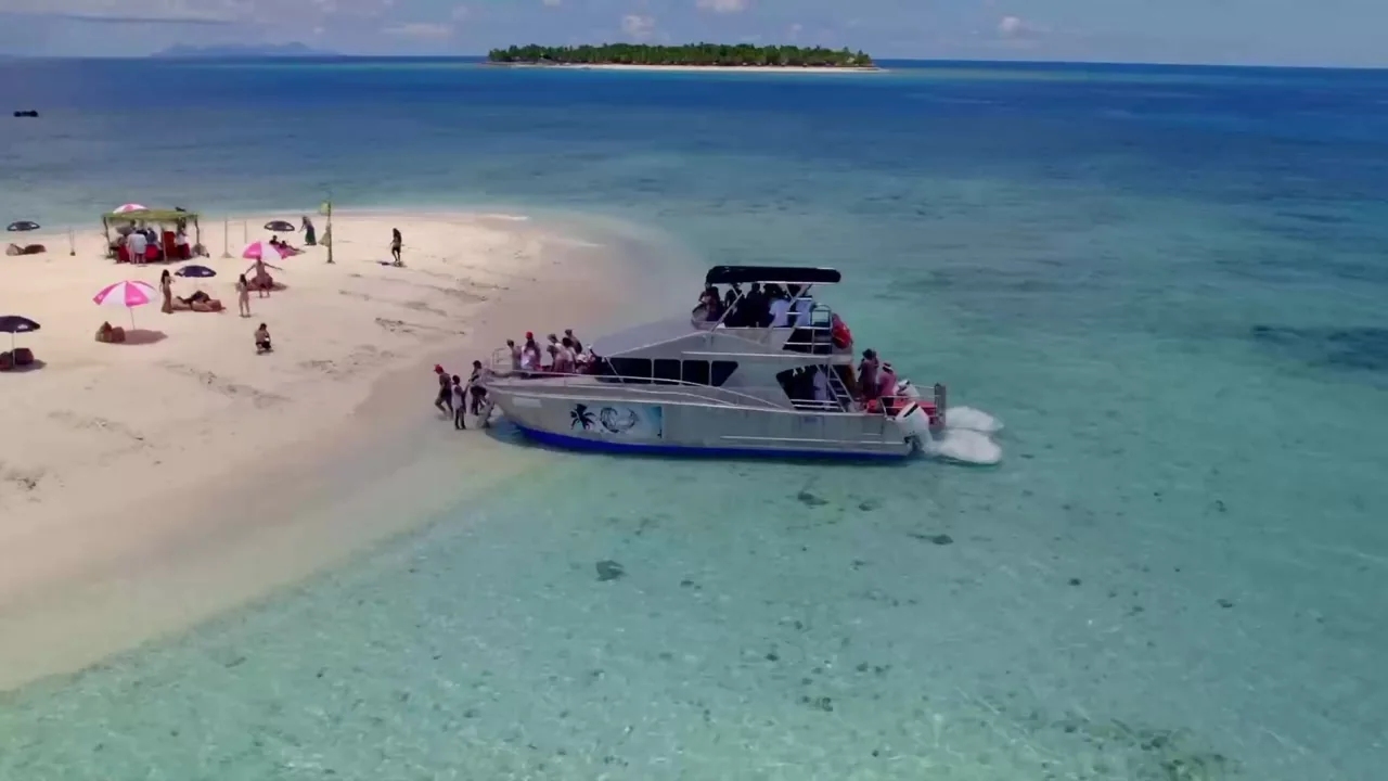 A boat beside a sandy island beach and turquoise water at Spring Break Fiji.